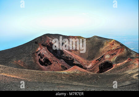 Volcanic crater on Mt Etna in Sicily, Italy - site of the 2002 eruption. Colourful  igneous rock, shades of red, amber and grey with hazy blue sky Stock Photo