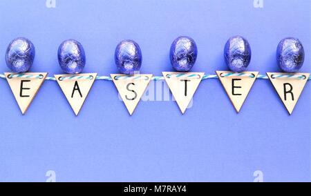 creative Easter concept with  shiny wrapped purple chocolate eggs. together with the word Easter, made from wooden triangles. purple colored backgroun Stock Photo