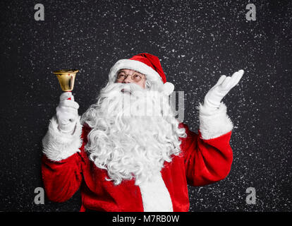 Santa claus with handbell among snow falling Stock Photo