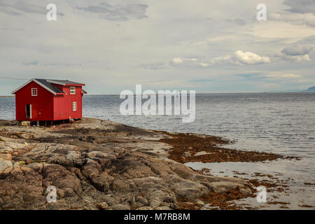 Small red cabin on the rocky shore of Ona Island - old fishing community in Sandoy Municipality in Western Norway, now an attractive tourist spot Stock Photo