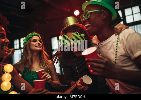 Group of young men and woman celebrating St. Patrick's Day. Friends having fun at the bar with green party glasses and hat. Stock Photo