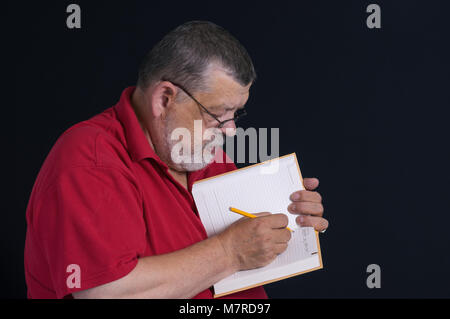 Nice low key portrait of a bearded senior writing a letter to his son in notebook Stock Photo