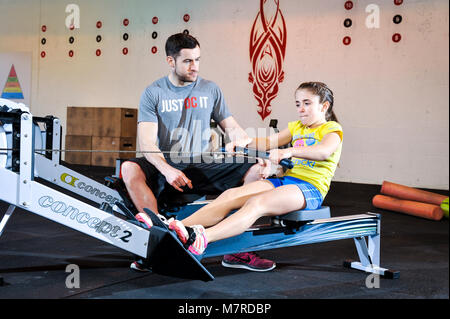 A young girl been given a lesson on a rowing machine in a gym. Stock Photo