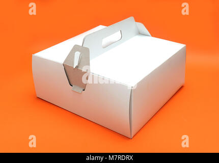 White closed cardboard cake box with handle on orange background Stock Photo