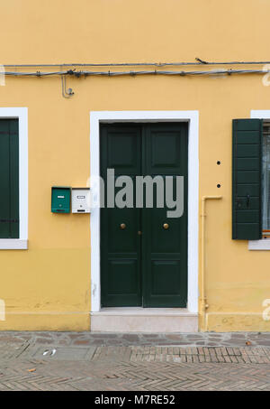 Green closed entrance door on old house with yellow stone facade Stock Photo