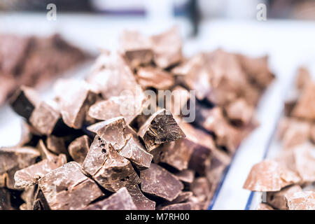 Pile of many milk dark brown chocolate pieces macro closeup chunks on tray glass display in candy shop store chocolatier Stock Photo