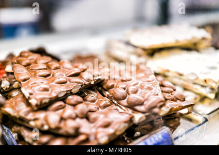 Macro closeup of pile of many milk dark brown chocolate bar almond nut peanut pieces chunks on tray glass display in candy store chocolatier shop Stock Photo