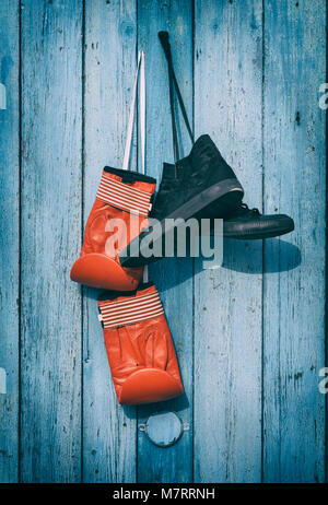 Black textile worn sneakers and red leather boxing gloves hanging on a blue wooden wall, vintage toning Stock Photo