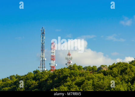 Three Telecommunication (GSM) towers with TV antennas ,satellite dishes and repeaters at the top of a hill on a blue sky and a cloud on background Stock Photo