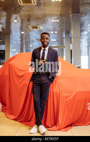 happy african car salesman using smart phone in showroom Stock Photo