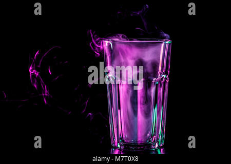 New glass with soft multi-colored  purple smoke from vape on a black isolated background Stock Photo