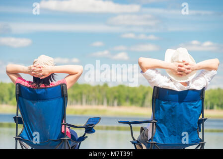 family on chairs resting near a beautiful lake on chairs, view from the back Stock Photo