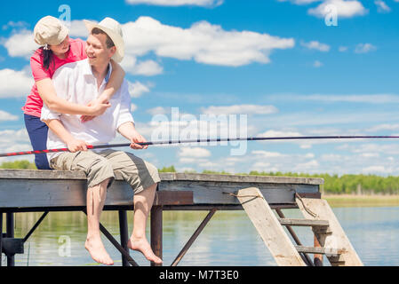 man with a fishing pole and his beloved woman on a wooden pier on a summer day Stock Photo