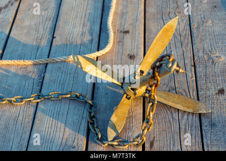 close-up anchor with chain in the rays of the morning sun lies on a wooden pier Stock Photo