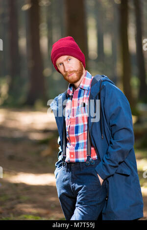 Vertical portrait of a stylish man with a beard wearing a hat and jacket posing in forest Stock Photo