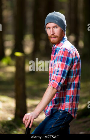 vertical portrait of a serious forester hipster with a beard with an ax in the woods Stock Photo