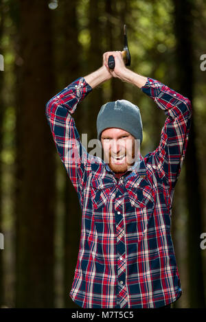 An aggressive bearded woodcutter with an ax chopping wood into the woods Stock Photo