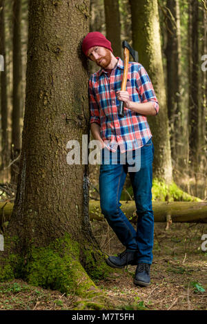 tired bearded lumberjack with an ax resting, leaning against a tree Stock Photo