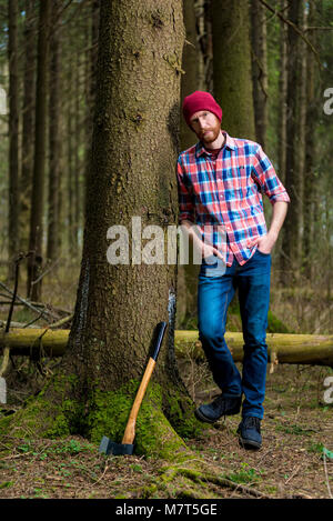 relaxed forester resting with an ax, leaning against a tree Stock Photo