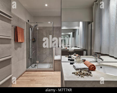 interiors shots of a modern bathroom in foreground the built-in washbasin and big mirror on the background the masonry shower cubicle with glass door, Stock Photo