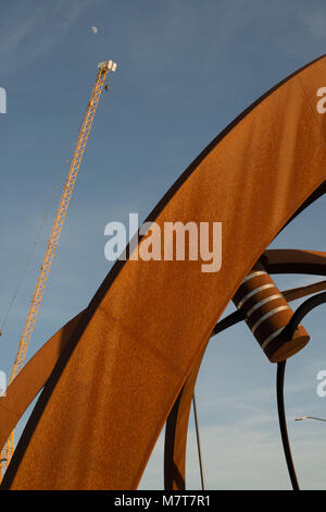 bright orange rusty sculpture with yellow tower crane and daylight moon in the background Stock Photo