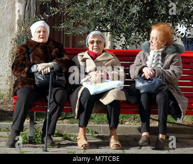Venice, Italy - January 22, 2018. Three elderly women sitting on the red bench under the tree in an inner atmospheric courtyard. Stock Photo