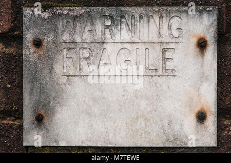 Weathered sign on brick wall saying WARNING FRAGILE Retouched for additional copy space. Stock Photo