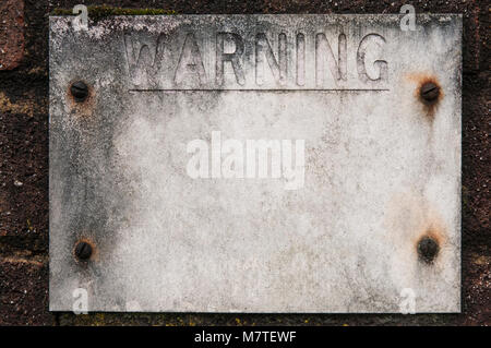 Weathered sign on brick wall saying WARNING. Retouched for additional copy space. Stock Photo