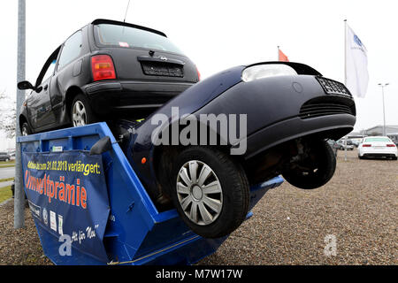 Schleswig, Germany. 13th March, 2018. Two cars stuck in a trash container. A Volkswagen dealership has installed the container in its premises as an eye-catcher for the topic of the environmental bonus for wrecking of old diesel cars. Photo: Carsten Rehder/dpa Credit: dpa picture alliance/Alamy Live News Stock Photo