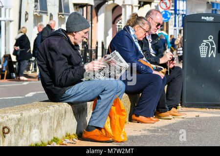 Sidmouth, Devon, UK.  13th March 2018.  UK Weather.  A man reading a newspaper on the seafront at the seaside town of Sidmouth in Devon on a warm sunny spring afternoon.  Picture Credit: Graham Hunt/Alamy Live News. Stock Photo