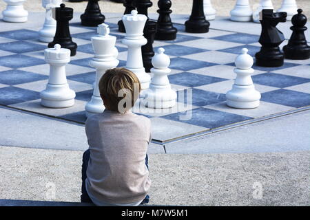Boy sitting down watching a chess game outside Stock Photo