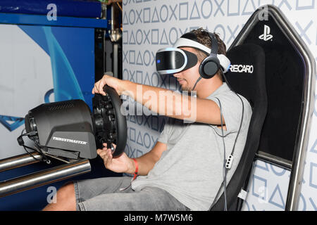 Cologne, Germany - August 24, 2017: A trade fair visitor is playing a racing game with vr headeset and special device at Gamescome 2017. Stock Photo