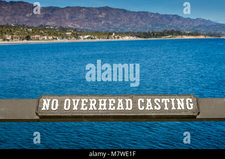 wooden sign on a brown railing saying No Overhead Casting at the Pacific Ocean in Santa Barbara, California, USA with mountains in the distance Stock Photo