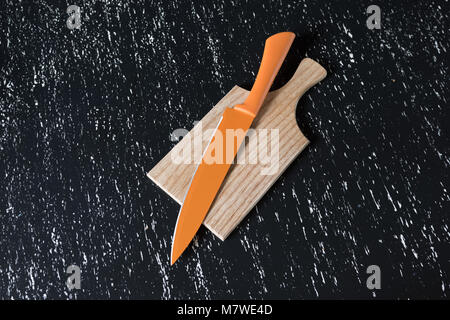 Big orange kitchen knife on wooden cutting board on black table. Stock Photo