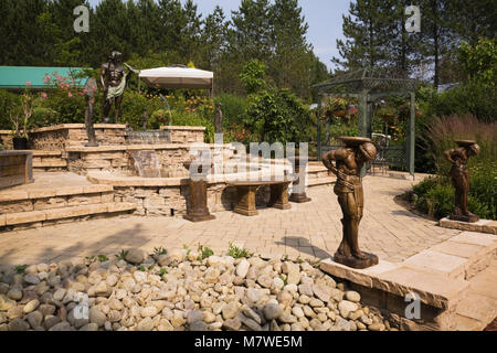 Light brown paving stone patio with cascading water fountain and tinted cement and bronze statues in backyard garden in summer Stock Photo