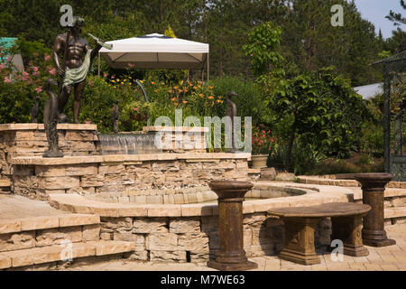 Light brown paving stone patio with cascading water fountain and tinted cement and bronze statues in backyard garden in summer Stock Photo