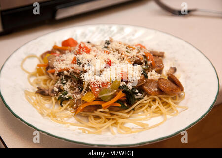 stir fry with sausage, vegetable and noodles prepared on a white kitchen plate Stock Photo