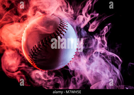 Colorful baseball ball in multi-colored red smoke from a vape on a black isolated background Stock Photo