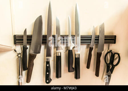 A set of high quality kitchen cook knives tools on a magnet board hanging on the wall Stock Photo