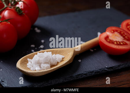 Seasoning vegetarian still life with fresh grape tomatoes, red pepper and cooking salt in wooden spoon on black piece of board over vintage wooden bac Stock Photo