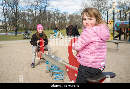 Two girls on a swing in a playground at springtime. Stock Photo