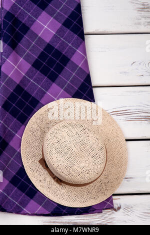 Wide brim straw summer hat. Purple checkered plaid clothes. Vertical cropped view. Stock Photo