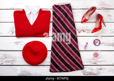 Red women's winter clothes look on wooden background. Flat lay. Folded shirt, sweater, shoes and cosmetic for make up. Stock Photo