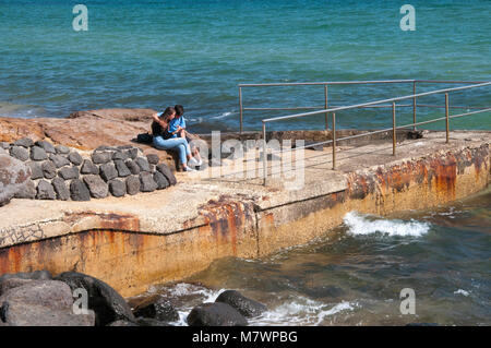 Teenaged couple sharing an intimate moment on a breakwater at Long Beach at Parkdale, Melbourne, Australia Stock Photo