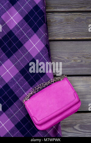 Top view purple handbag and checkered skirt. Grey wooden surface background. Stock Photo