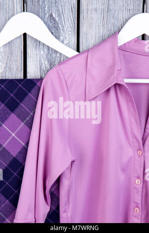 Close up purple silk clothes on hangers. Dark wooden desk surface background. Stock Photo