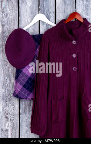 Flat lay violet winter clothing. Woolen coat and skirt on hanger. Dark wooden desk surface background. Stock Photo