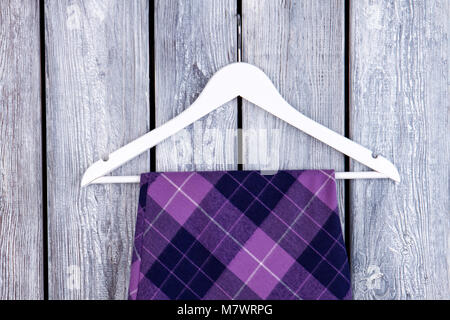 Close up hanger and purple checkered clothes. Woolen violet skirt on wooden desk surface background. Stock Photo