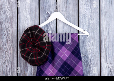 Purple checkered skirt and black hat, top view. Flat lay, female clothes on dark wooden desk background. Stock Photo