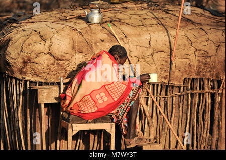 Sunset in an African village - portrait of a brightly robed, Samburan warrior, seated by his manyatta (traditional mud hut). Stock Photo